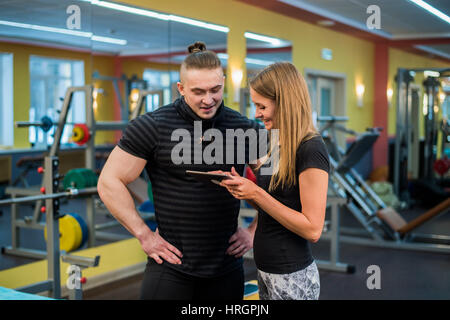 Passen Sie attraktives junges Paar in einem Fitnessstudio, einem Tablet-pc zu betrachten, wie sie ihre Fortschritte und Fitness überwachen Stockfoto