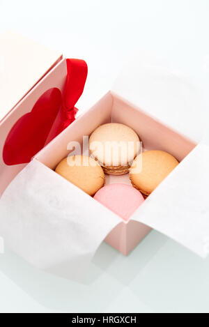 4 bunte Makronen in den Valentinstag Themen rosa Feld mit roten Herzen und Bogen auf der Box verpackt. Stockfoto