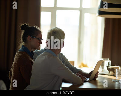 Seite Ansicht Bildniss mehrere kreative Geschäftsleute sitzen zusammen am Tisch im dunklen Raum, Gespräch zu treffen und mit Blick auf Laptop-Bildschirm Stockfoto