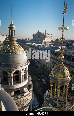 Die reich verzierten Kuppeln der das Kaufhaus Galeries Lafayette in der Wintersonne glänzen mit der Palais Garnier-Oper in der Ferne. Stockfoto