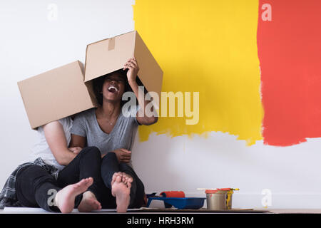 Glückliche junge multiethnischen paar entspannen und spielen mit Kartons nach einen Raum in ihrem neuen Haus auf dem Boden zu malen Stockfoto