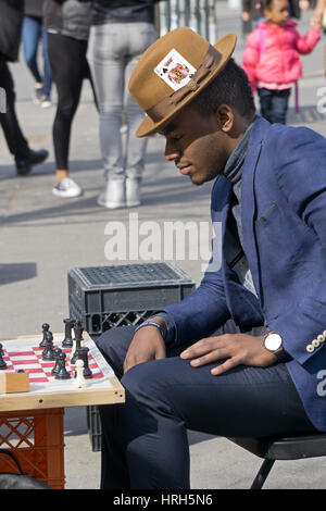 Ein schreitend gekleideter Mann mit einem Pik-Ass-Karte in seinen Hut spielen Schach am Union Square Park in Manhattan, New York City. Stockfoto