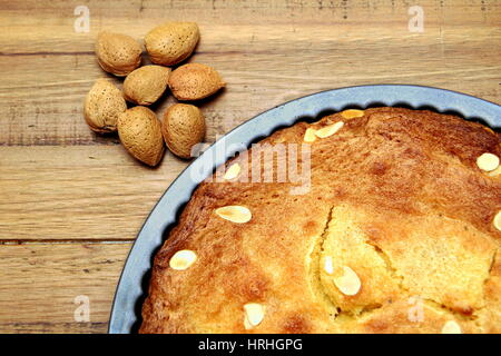 Ungeschälte Mandeln Nüssen neben einem frisch gebackenen Frangipane-Torte oder Kuchen Stockfoto