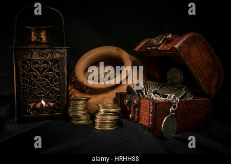 Schatztruhe, Stapel und Säule der Münzen, eine Keramikschale voller Schmuck Münzen und Kerze Lampe in dunkler Umgebung Stockfoto