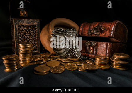 Schatztruhe, Stapel und Säule der Münzen, eine Keramikschale voller Schmuck Münzen und Kerze Lampe in dunkler Umgebung Stockfoto