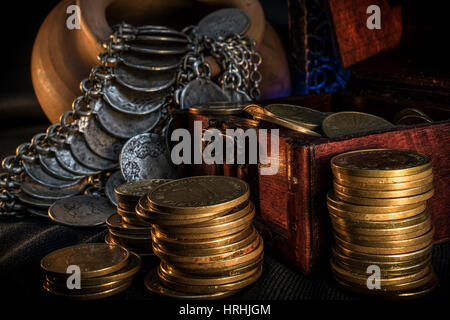 Schatztruhe, Stapel und Säule der Münzen, eine Keramikschale voller Schmuck Münzen und Kerze Lampe in dunkler Umgebung Stockfoto