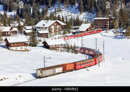 Roter Zug der Rhätischen Bahn geht in die verschneite Landschaft von Arosa, Bezirk Plessur, Kanton Graubünden, Schweiz Stockfoto