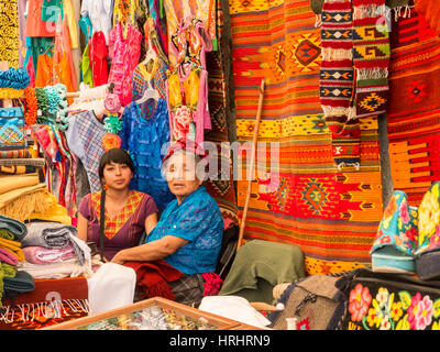 Frauen reden im Markt mit Hintergrund handgeknüpfte Teppiche und Kleidung, Oaxaca, Mexiko, Nordamerika Stockfoto