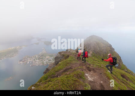 Wanderer auf felsigen Gipfel bewundern das blaue Meer, umgeben von Nebel, Reinebringen, Moskenesoya, Lofoten Inseln, Norwegen Stockfoto