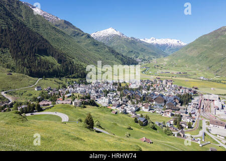 Das alpine Dorf Andermatt, umgeben von grünen Wiesen und schneebedeckten Gipfeln im Hintergrund, Kanton Uri, Schweiz Stockfoto