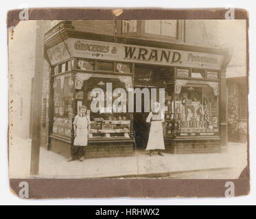 Original Schwarz-weiß-Foto Anfang der 1900er Jahre viktorianisches Geschäft oder edwardianisches Geschäft, Foto des Besitzers mit seinem jungen Assistenten / Personal vor einem Lebensmittel- und Provisionsgeschäft, W. Rand, ein unabhängiges Eckgeschäft, in einer britischen Stadt, Großbritannien Stockfoto