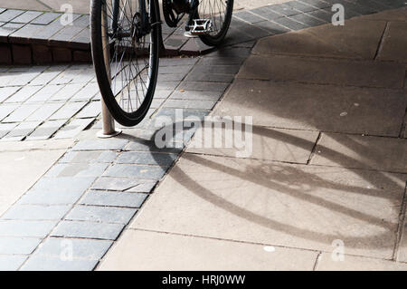 Fahrrad eingesperrt und wirft einen Schatten auf dem Bürgersteig Stockfoto