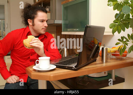 Junger Mann Zuhause Isst Einen Burger w? Hrend der Arbeit am Laptop Stockfoto