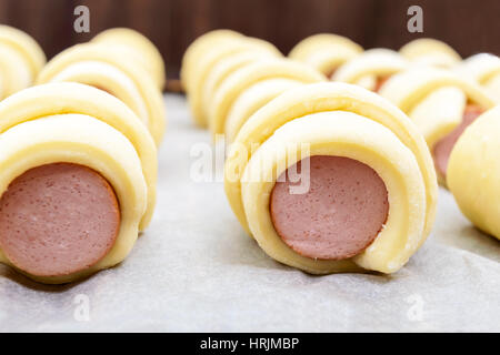 Home Baking: Würstchen im Teig. Viele rohe Brötchen auf dem Gitter. Nahaufnahme Stockfoto