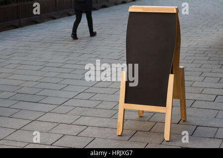 horizontale leere schwarze hölzerne Restaurant Bürgersteig Tafel auf einer Straße mit Passanten Stockfoto