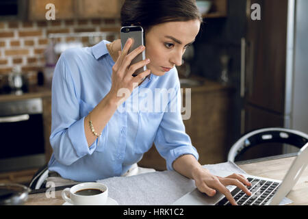 Konzentrierte sich die junge Frau am Smartphone während mit laptop Stockfoto