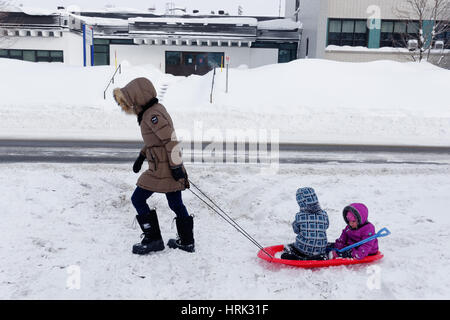 Eine Mutter zieht ihre beiden Kinder in einem Schlitten durch Neuschnee in Quebec im winter Stockfoto