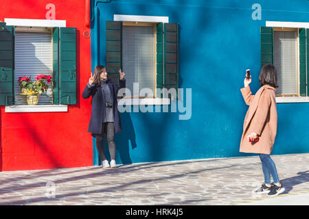 Weibliche Touristen posiert für ein Foto vor hellen blauen und roten Häusern in Burano - leuchtenden Farben der Burano, Venedig, Italien im Januar Stockfoto