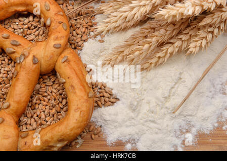 Körner, Ähren, Mehl und Brezel auf einem Holztisch. Konzept der Zubereitung von Essen aus Getreide, Rohstoff im fertigen Produkt. Rustikaler Hintergrund. Stockfoto