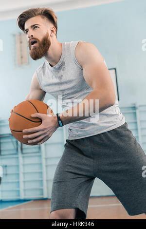 Bärtiger junger sportlicher Mann spielen Basketball im Sportzentrum Stockfoto