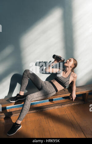 sportliche Frau auf der Bank Trinkwasser aus Sport-Flasche Stockfoto