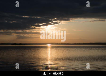 Sonnenuntergang über dem Wasser verbirgt sich hinter Wolken Stockfoto