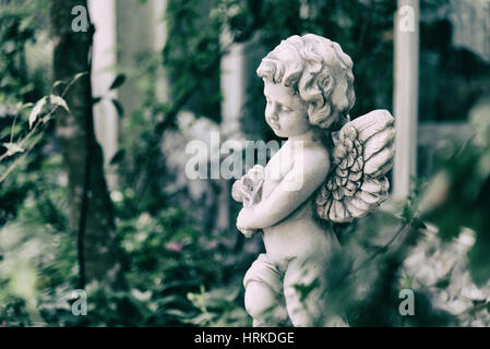 Schönheit Amor Statue des Engels in Vintage Garten im Sommer. Bouquet Blumen hält in der hand Stockfoto