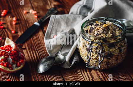 Glas mit Müsli, geöffnete Granatapfel und einige Besteck. Stockfoto