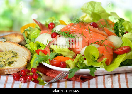 Frische Sommer-Salat mit Honigmelone Kugeln und geräucherter Wildlachs, serviert mit geröstetem Ciabatta-Brot mit Kräuterbutter Stockfoto