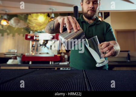 Das Barkeeper Barista gießt heißen Milch in ein Glas in bar-café Stockfoto