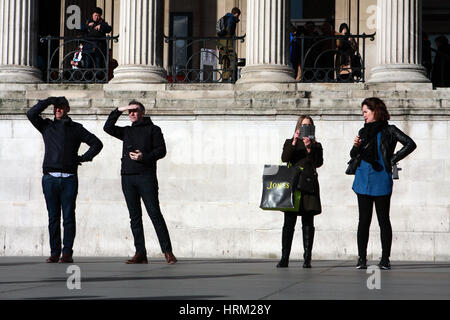 Vier Personen stehen in einer Reihe vor der National Gallery am Trafalgar Square in London, England. Stockfoto