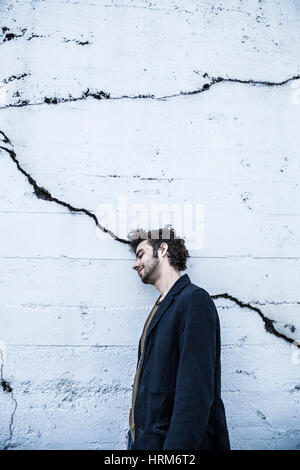 Ein Portrait eines jungen Mannes grinsend und eine rissige Wand gelehnt. Stockfoto