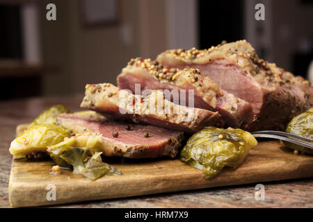 Geschnittene corned Rindfleisch auf einem Holzbrett garniert mit Pfefferkörnern und Brussel Sprossen als eine Party Teller servierfertig Stockfoto