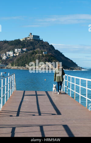 Spanien: Frau mit einem Hund auf dem Pier in Donostia-San Sebastián mit Blick von der Strand La Concha, gilt als eines der besten Stadtstrände in Europa Stockfoto