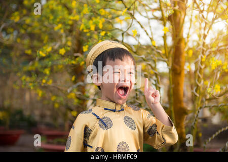 Glückliches Kind Spaß mit traditioneller Kleidung (Ao Dai) im Ochna Integerrima (Hoa Mai) Garten. Hoa Mai Blume dient zur Dekoration im neuen Mondjahr in Stockfoto