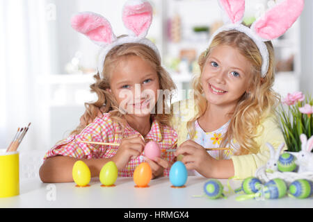 Niedliche zwei Schwestern tragen Hasenohren und Bemalen von Ostereiern zu Hause Stockfoto