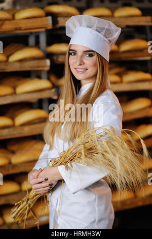 hübsche blondes Mädchen hält in Händen Ähren auf Hintergrund Bäckerei Stockfoto