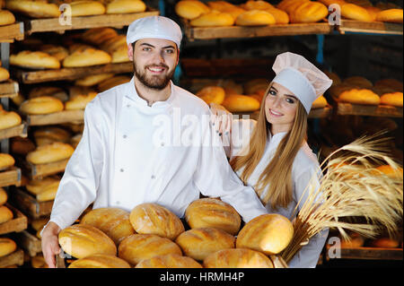 junger Mann und Frau in uniform Bäcker mit Ährchen des Weizens in den Händen auf dem Hintergrund der Bäckerei Stockfoto