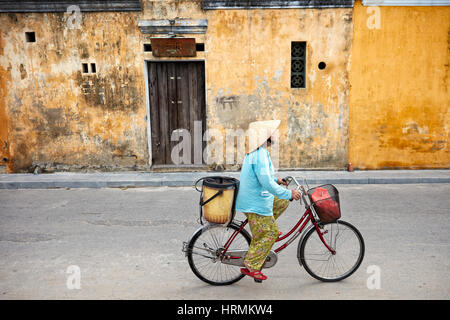 Vietnamesische Frau in traditionellen konischen hat Reiten Fahrrad in der alten Stadt Hoi An. Die Provinz Quang Nam, Vietnam. Stockfoto