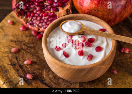 Joghurt mit Granatäpfeln in Holzschale auf rustikalen Tisch. Stockfoto