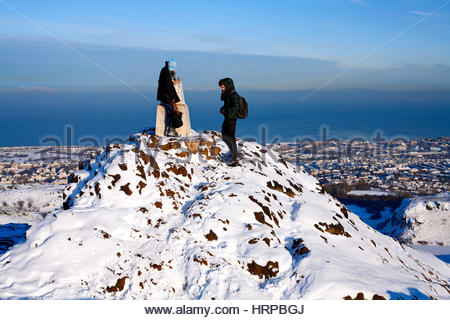 Zwei Wanderer auf Arthurs Seat, Edinburgh im Winter mit Blick über die Stadt im Norden und Fluss Forth Stockfoto