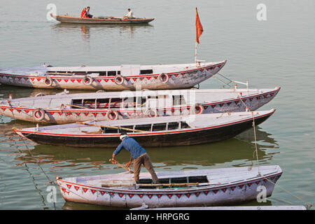 Bootsmann und eine kleine Flotte von touristischen Boote vertäut am Ufer des Flusses Ganges in Varanasi, Indien. Stockfoto