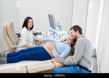 Eltern Kind und in moderne Klinik, Diagnose erste Foto von Baby betrachten. Arzt mittels Ultraschall, schwangeren Frau lächelnd Sieb- Stockfoto