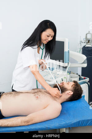 Lächelnde Ärztin durchführen Schilddrüsen-Ultraschall-Test auf männliche Patienten im Krankenhaus Stockfoto