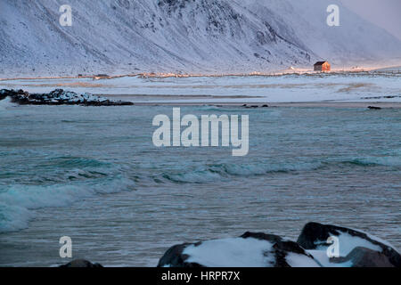 Norwegen. Lofoten. Winter in der Nähe von Ramberg. Berge und Surf. Ein Sonnenstrahl beleuchtet einem einsamen Haus Stockfoto