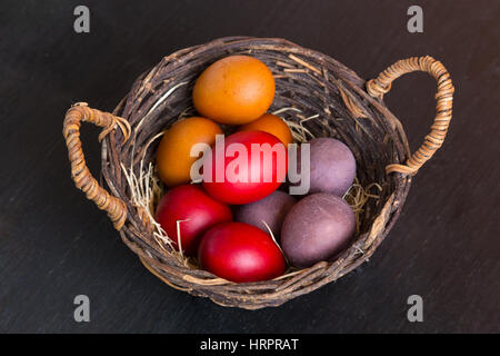 Weidenkorb mit bunten Ostern Eiern auf Holztisch, Nahaufnahme Stockfoto