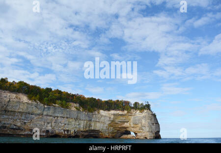 An der Unterseite des Rahmens ragt eine Felsformation mit einem Bogen am Ende ins Wasser an einem sonnigen Tag mit Wolken am Himmel. Stockfoto