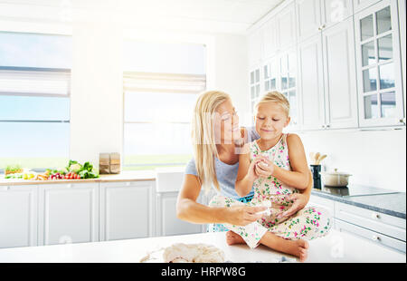 Mädchen sitzen am Küchentisch mit Brotteig neben aufgeregt Mutter Spaß Stockfoto