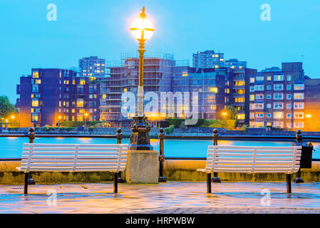 Riverside Bänke in der Nacht mit Schwerpunkt Gebäude in der Ferne Stockfoto