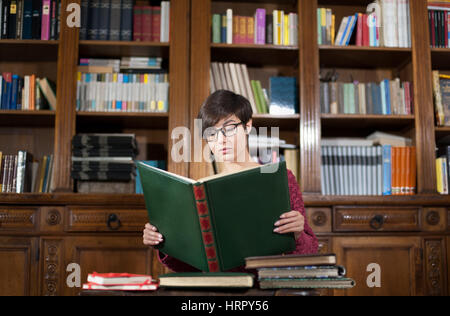 Junge Studentin mit absorbiert Gesichtsausdruck beim Lesen Buch in der Bibliothek Stockfoto